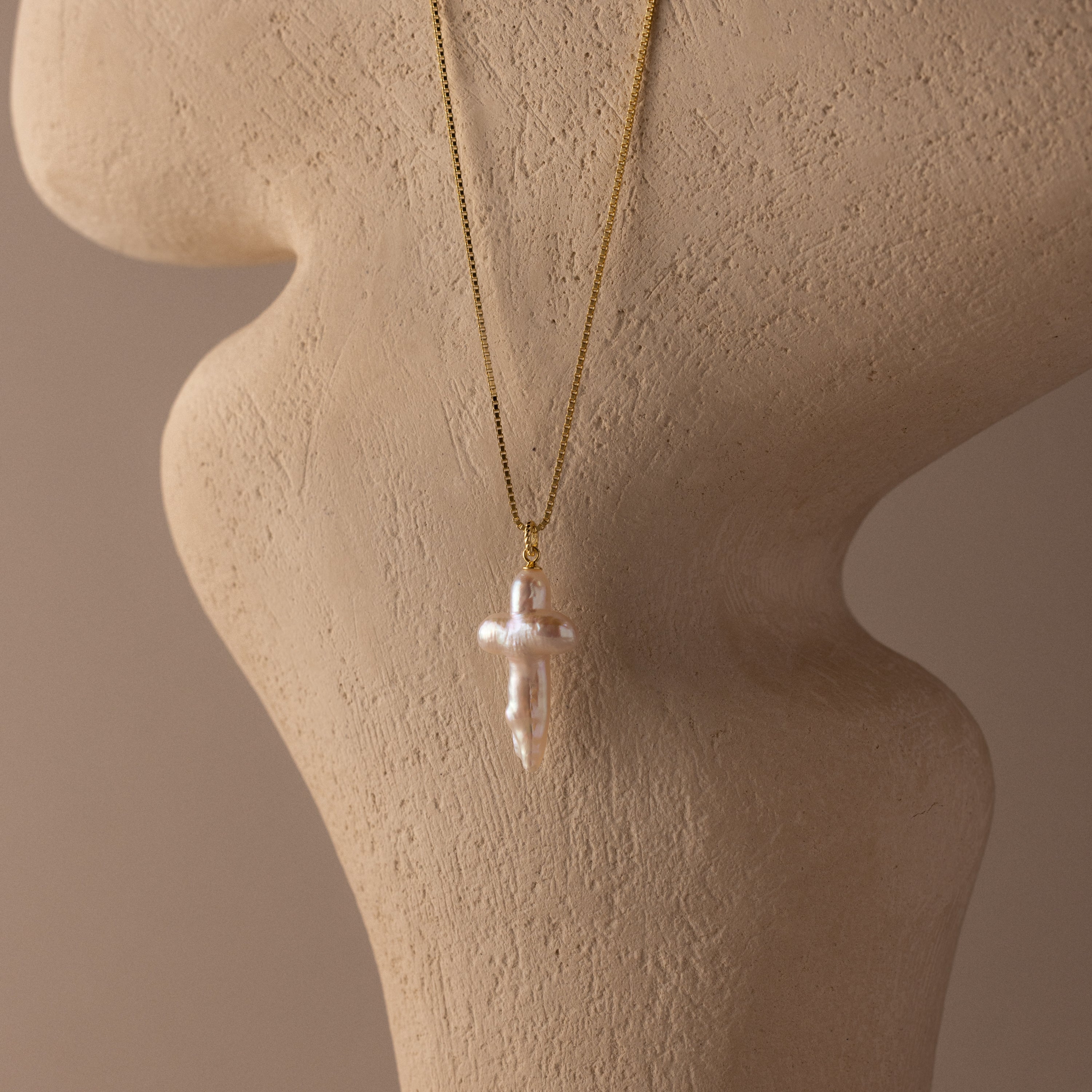 Baroque Pearl Cross Necklace in 18K Gold displayed on a beige textured mannequin bust.