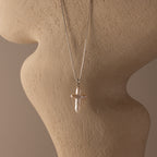 The Baroque Pearl Cross Necklace showcases a pearl cross pendant on a silver chain, elegantly displayed on a beige textured mannequin bust.