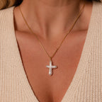 A woman wears the Baroque Pearl Cross Necklace featuring a white cross-shaped pendant over a cream knit top.