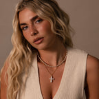 A woman with wavy blonde hair wears a cream knit top and the Baroque Pearl Cross Necklace in 18K Gold, looking at the camera.