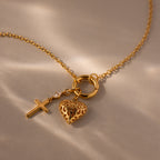 Diamond Drop Cross Charm in 18K Gold, featuring a cross pendant with heart charm and diamond accent, shown against a soft beige background.