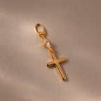 Diamond Drop Cross Charm in 18K Gold, featuring a small diamond accent, displayed on a light beige background.