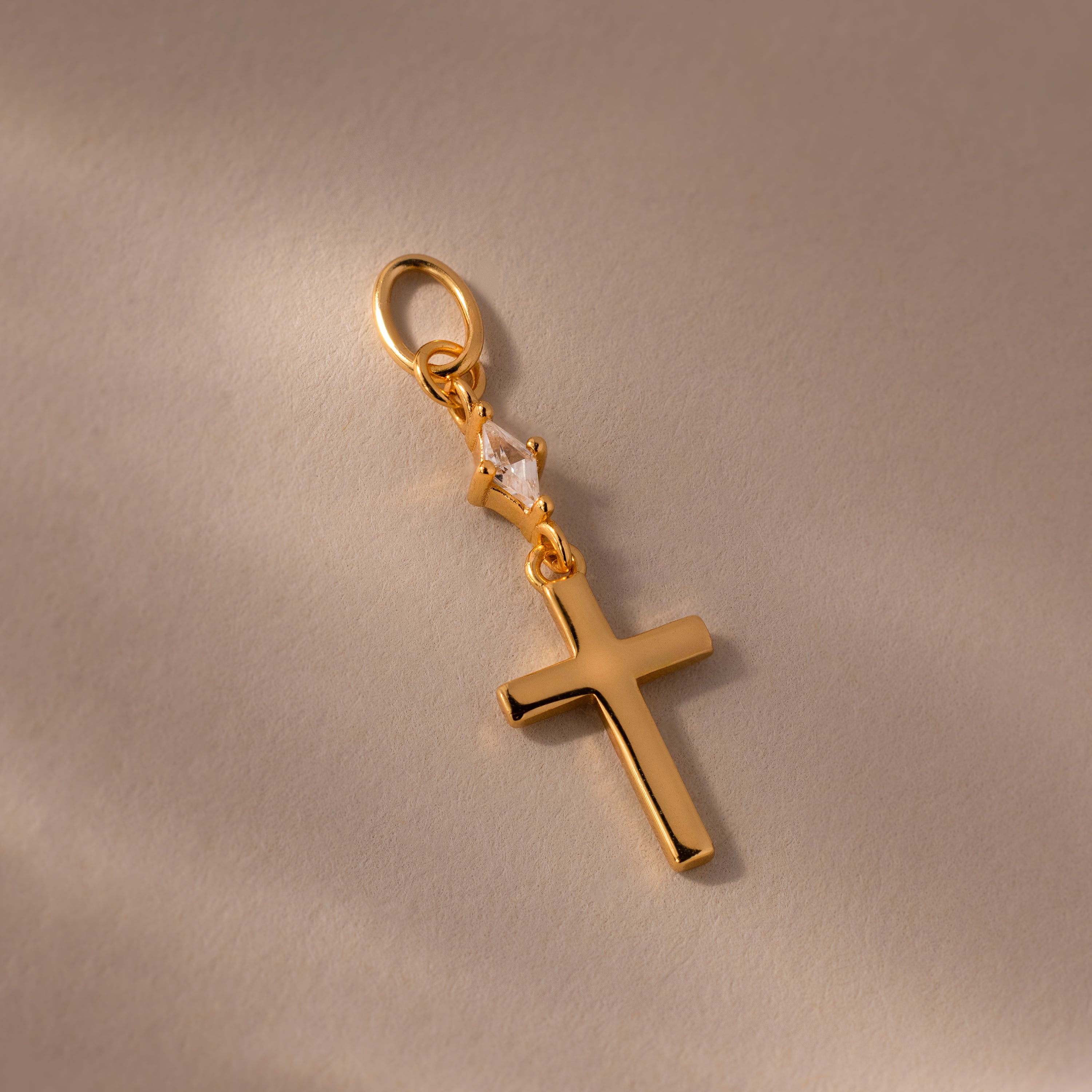 Diamond Drop Cross Charm in 18K Gold, featuring a small diamond accent, displayed on a light beige background.