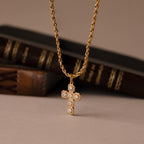The Majesty Cross Necklace features a gold chain and diamond-studded cross pendant, showcased before vintage books—ideal for those seeking elegant faith jewelry.
