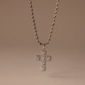 Majesty Cross Necklace in Silver featuring a diamond-encrusted cross pendant and sparkling stones, displayed on a neutral beige background.