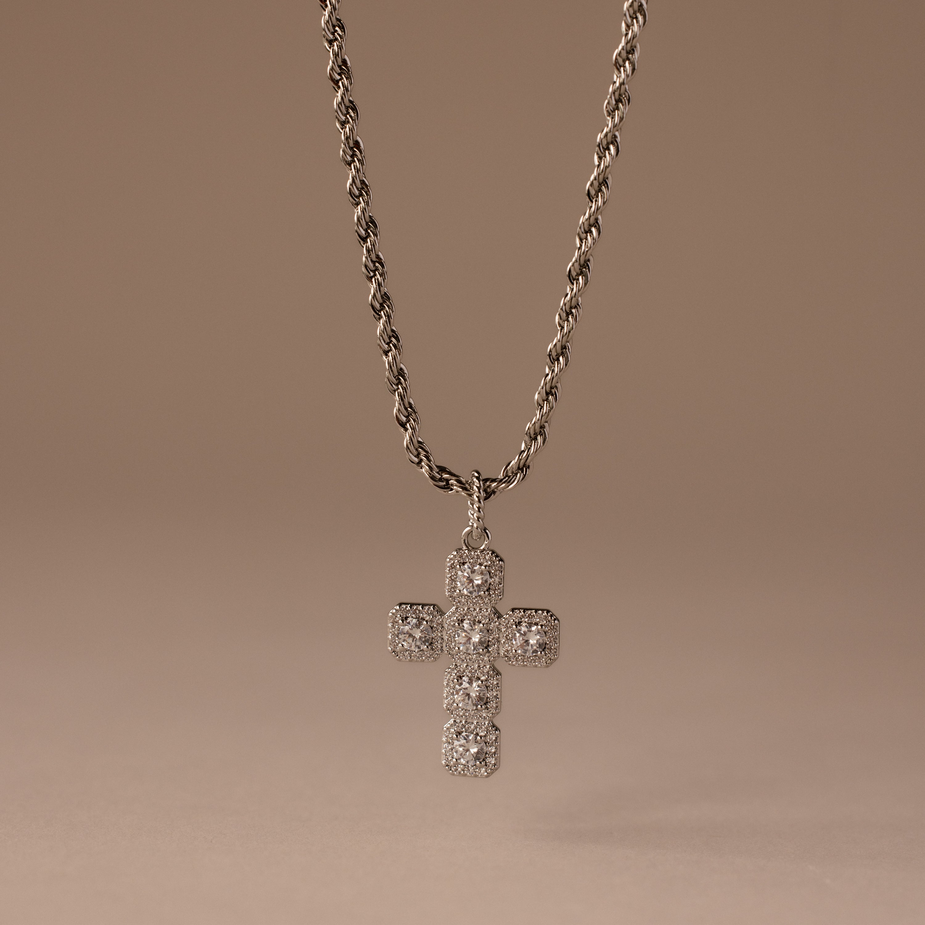 Majesty Cross Necklace in Silver featuring a diamond-encrusted cross pendant and sparkling stones, displayed on a neutral beige background.