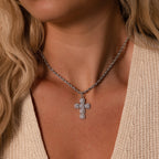 A woman wearing the Majesty Cross Necklace with a silver pendant over a cream knit top.