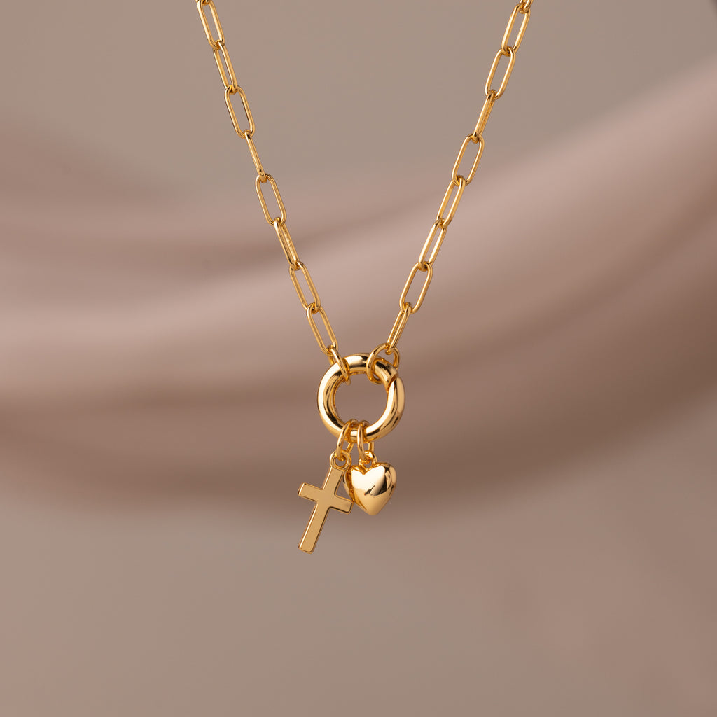 Cross & Heart Charm Bracelet in 18K Gold, featuring cross and heart charms on a stylish paperclip chain, displayed against a soft beige background.