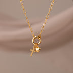 Cross & Heart Charm Bracelet in 18K Gold, featuring cross and heart charms on a stylish paperclip chain, displayed against a soft beige background.