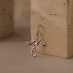 The Infinity Cross Charm in Silver, symbolizing eternal faith, rests against a beige textured stone surface.