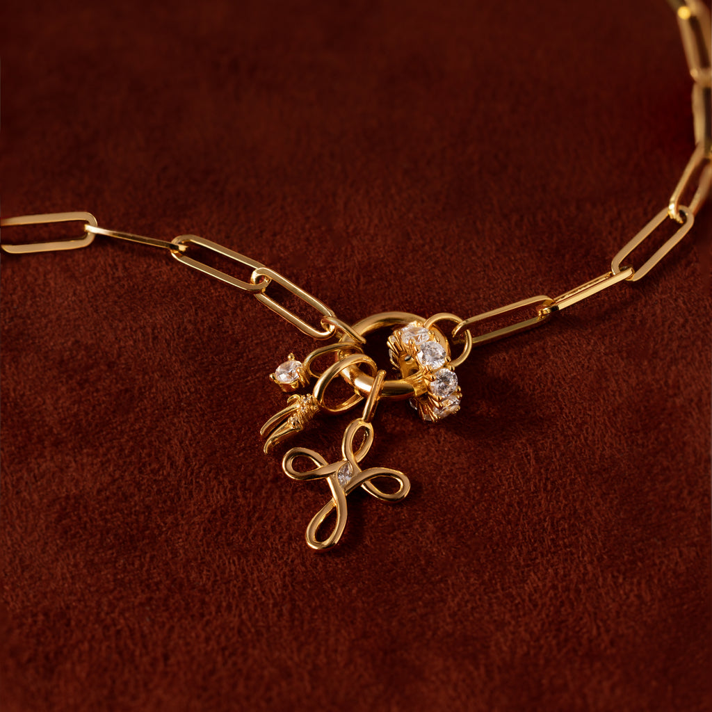 The Infinity Cross Charm necklace, featuring a gold chain and diamond floral charms, symbolizes eternal faith and is displayed on a brown velvet background.