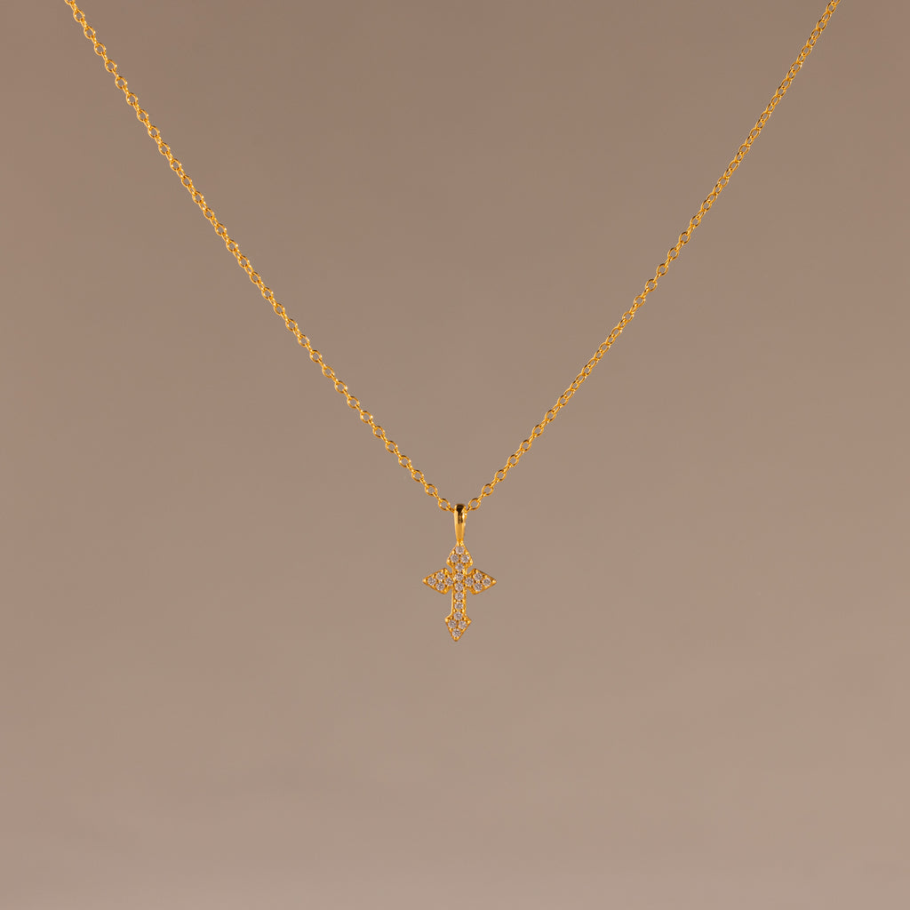 The Vintage Cross Necklace in 18K Gold features a pavé-finished, diamond-studded cross pendant displayed on a simple light brown background.