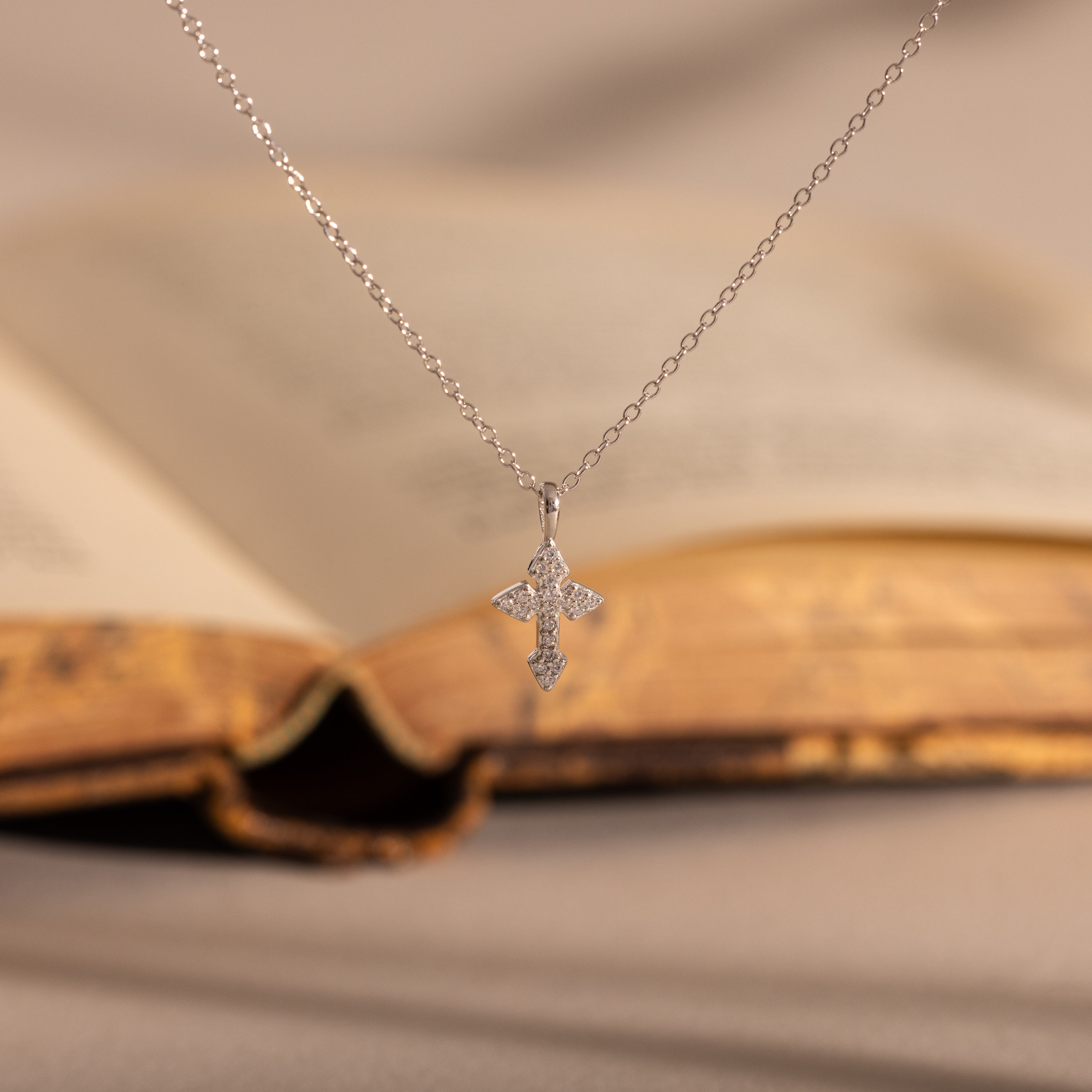The Vintage Cross Necklace features a pavé finish with small diamonds, shown in front of an open vintage book.