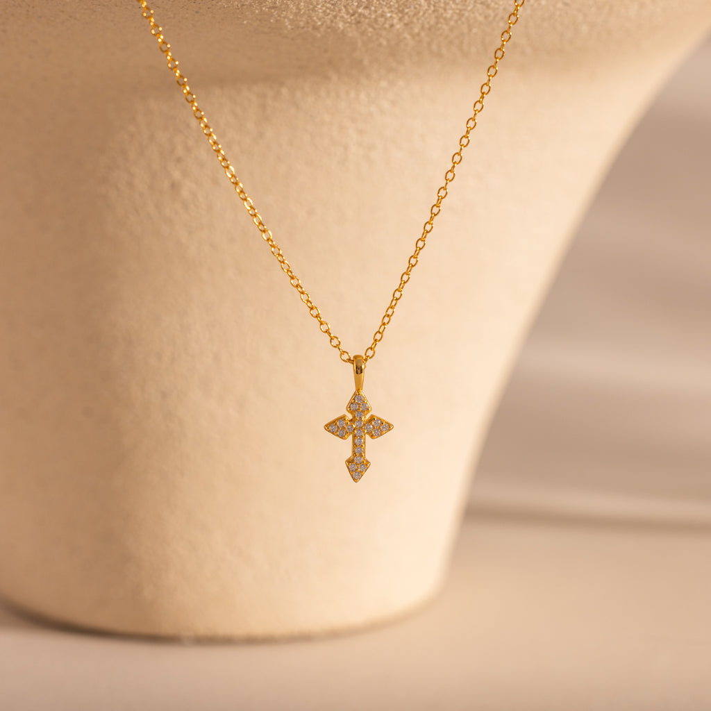 The Vintage Cross Necklace in 18K Gold features a minimalist chain and a pavé diamond-studded cross pendant, elegantly shown on a beige background.