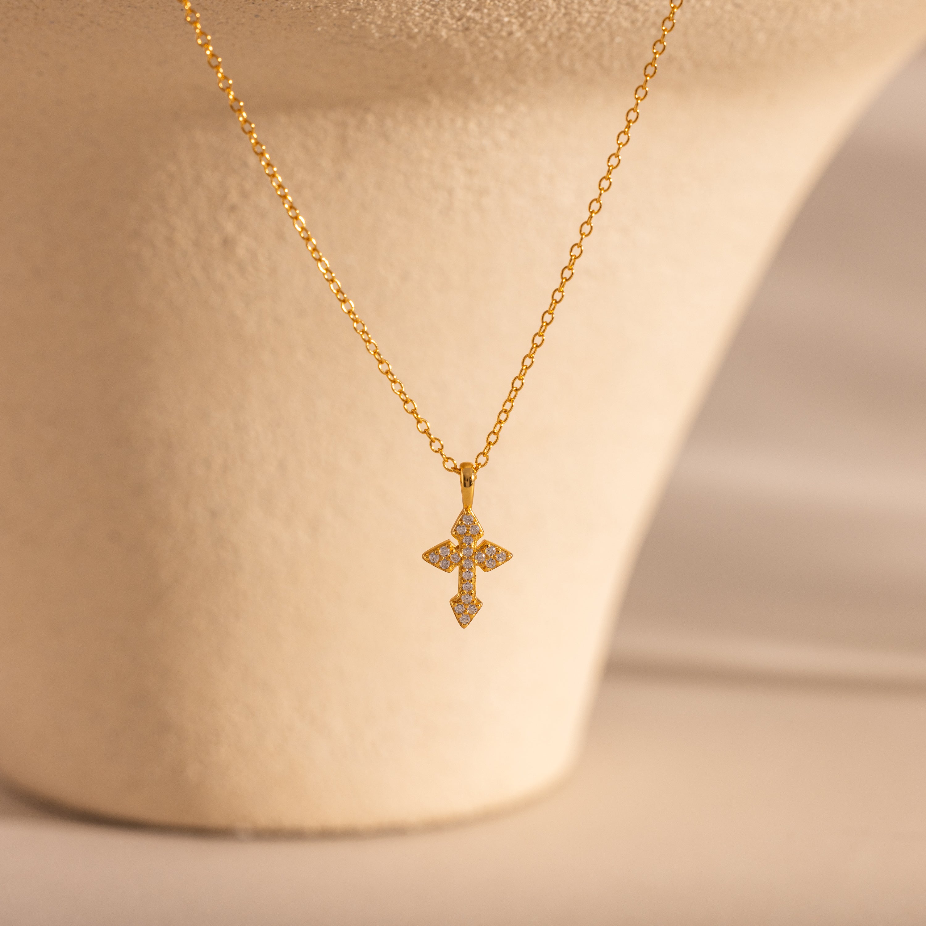 The Vintage Cross Necklace in 18K Gold features a minimalist chain and a pavé diamond-studded cross pendant, elegantly shown on a beige background.