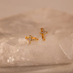 Two Diamond Cross Huggies featuring gold and pavé diamonds rest on a translucent, textured crystal slab.