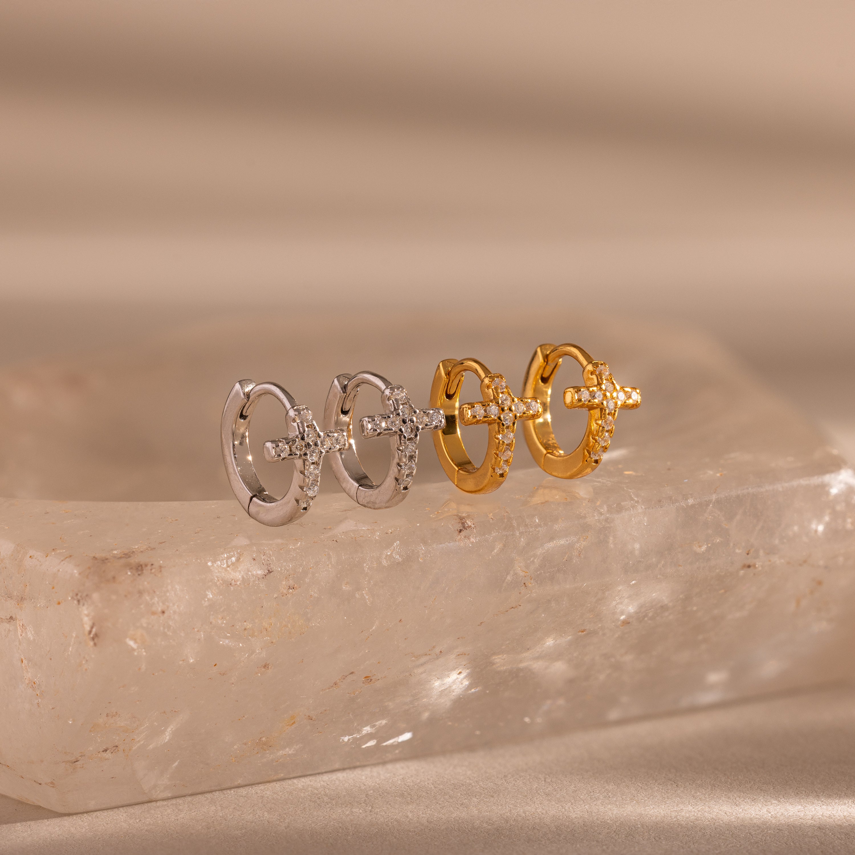 Two pairs of Diamond Cross Huggies, one in silver and one in gold, each featuring pavé stones on the cross charms, displayed on a stone slab.