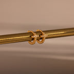 Diamond Cross Huggies in 18K Gold, featuring cross designs and pavé stones, hang on a metallic rod against a neutral background.