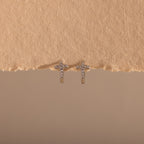 Diamond Cross Huggies in Silver sparkle with pavé stones, displayed against a textured beige background.