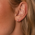 Close-up of a woman's ear wearing Diamond Cross Huggies in 18K Gold, each with a delicate cross pendant and sparkling pavé stones.