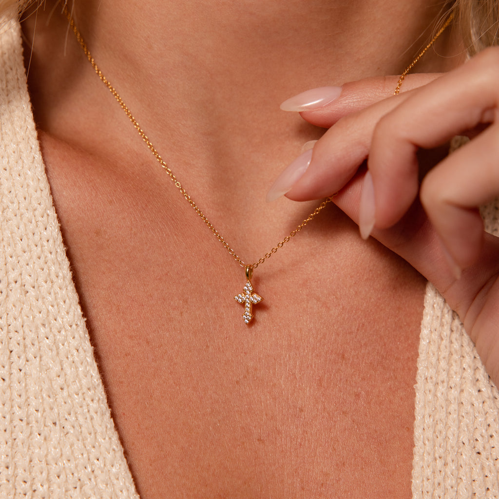 A woman wearing the Vintage Cross Necklace in 18K Gold with a pavé finish cross pendant and a beige knit top.