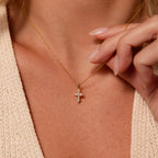 A woman wearing the Vintage Cross Necklace in 18K Gold with a pavé finish cross pendant and a beige knit top.