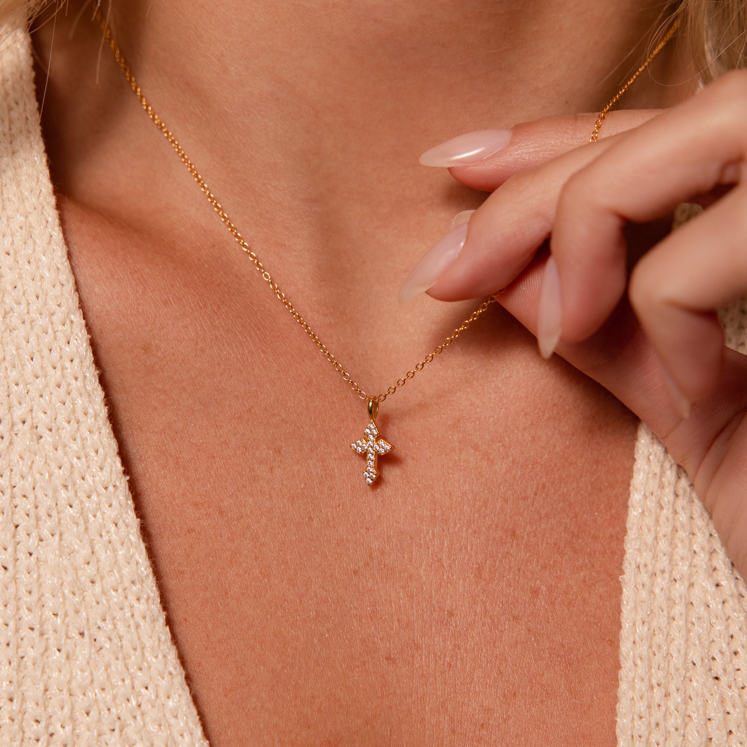 A woman wearing the Vintage Cross Necklace in 18K Gold with a pavé finish cross pendant and a beige knit top.