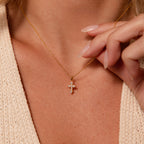 A close-up of a woman wearing the Vintage Cross Necklace with a pavé finish and small diamond pendant as she delicately holds its chain.