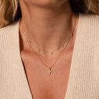 Woman wearing two delicate gold necklaces—a minimalist piece and the Vintage Cross Necklace in 18K Gold with pavé finish—over a beige textured top.