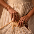 Woman in a white lace dress holds a lace fan, showcasing summer elegance with gold rings, bracelets, and a chic Pearl Hand Chain Bracelet.