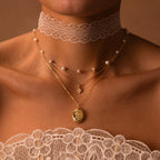 Woman wearing a lace choker, pearl necklace, gold chains, and the Floral Handwriting Locket Necklace with a lace-trimmed top against a brown background.