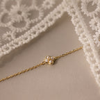 Experience delicate elegance with the Rounded Pearl Flower Bracelet in 18K Gold—featuring a small pearl flower pendant on a fine gold chain, beautifully displayed on cream fabric with lace edging.
