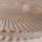 Rounded Pearl Flower Studs feature a gold bezel floral design accented with small pearls—ideal as bridesmaid jewelry—shown on a ridged, translucent surface.