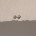 The Rounded Pearl Flower Studs in Sterling Silver, featuring pearl-like centers, are displayed on a textured off-white surface—an elegant choice for bridesmaid jewelry.