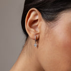 Close-up of a woman’s ear wearing Pave Rounded Pearl Flower Hoops in Sterling Silver, featuring delicate floral-shaped pendants—perfect as elegant wedding jewelry.