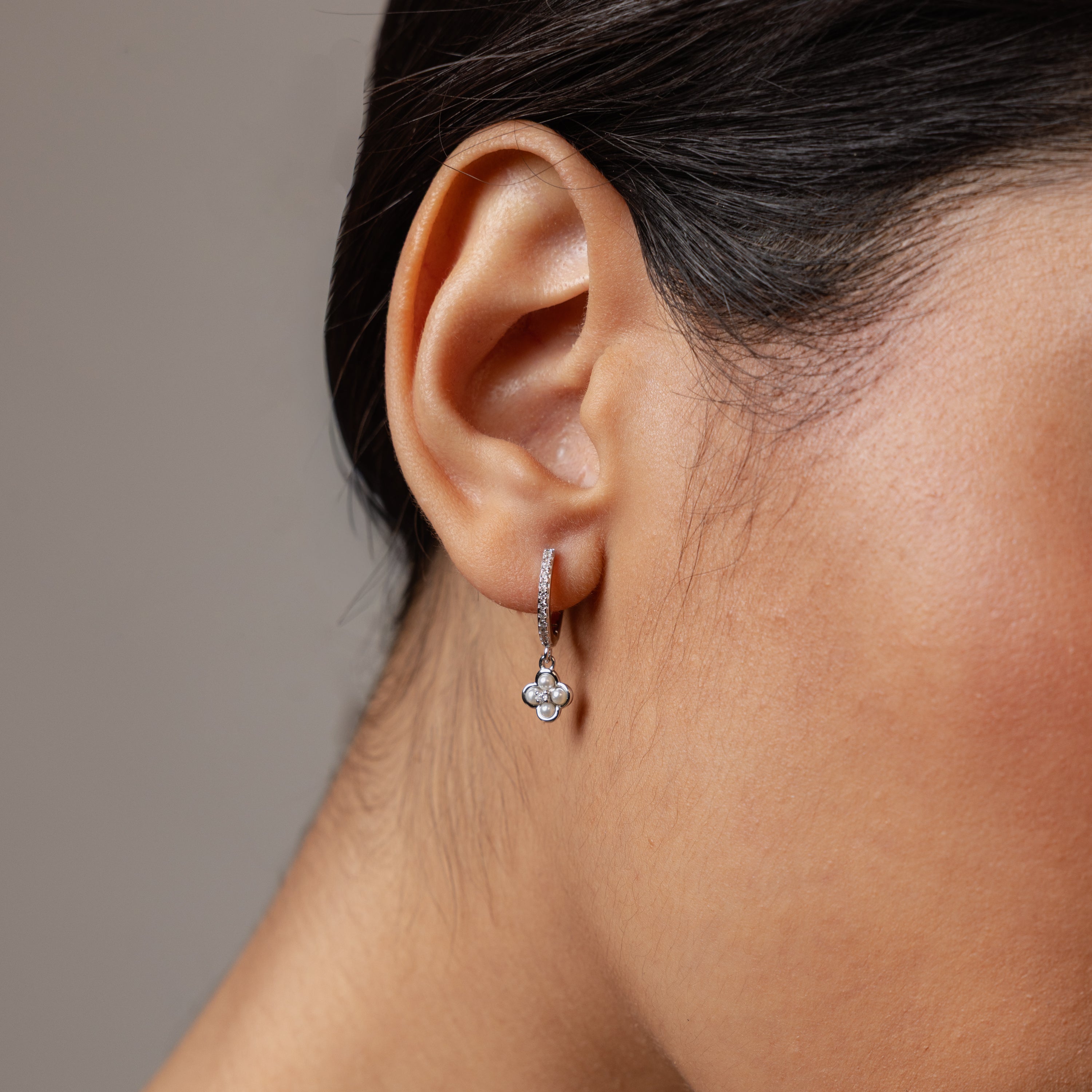 Close-up of a woman’s ear wearing Pave Rounded Pearl Flower Hoops in Sterling Silver, featuring delicate floral-shaped pendants—perfect as elegant wedding jewelry.