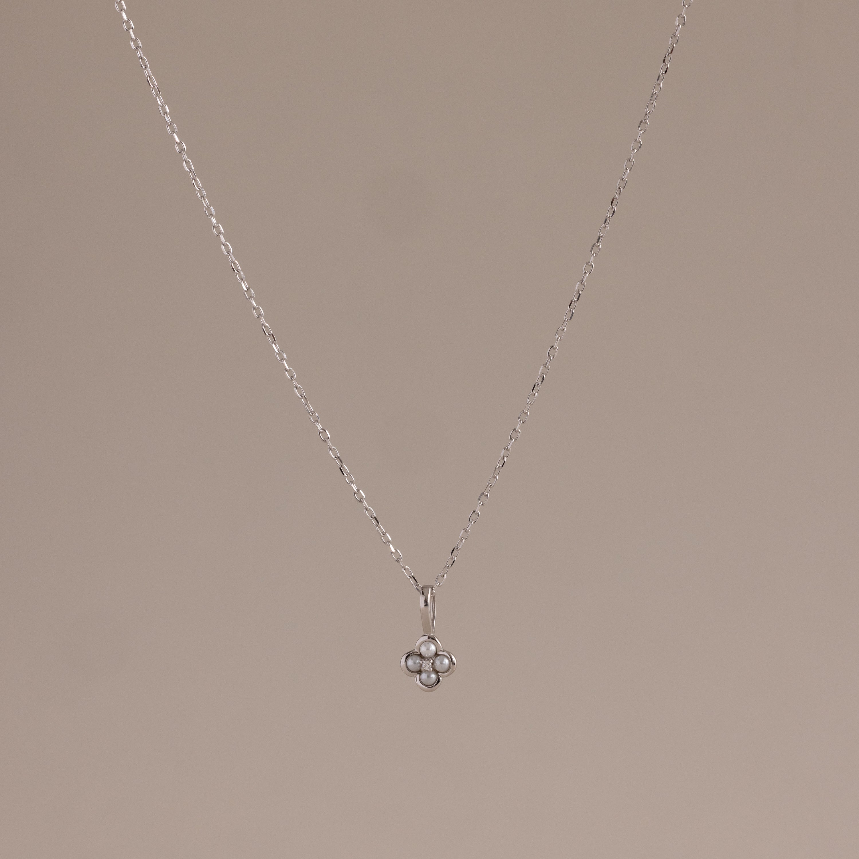 The Rounded Pearl Flower Necklace in Sterling Silver features a delicate chain and a small, three-pearl floral pendant, perfect for everyday layering and adding subtle elegance to any neutral background.