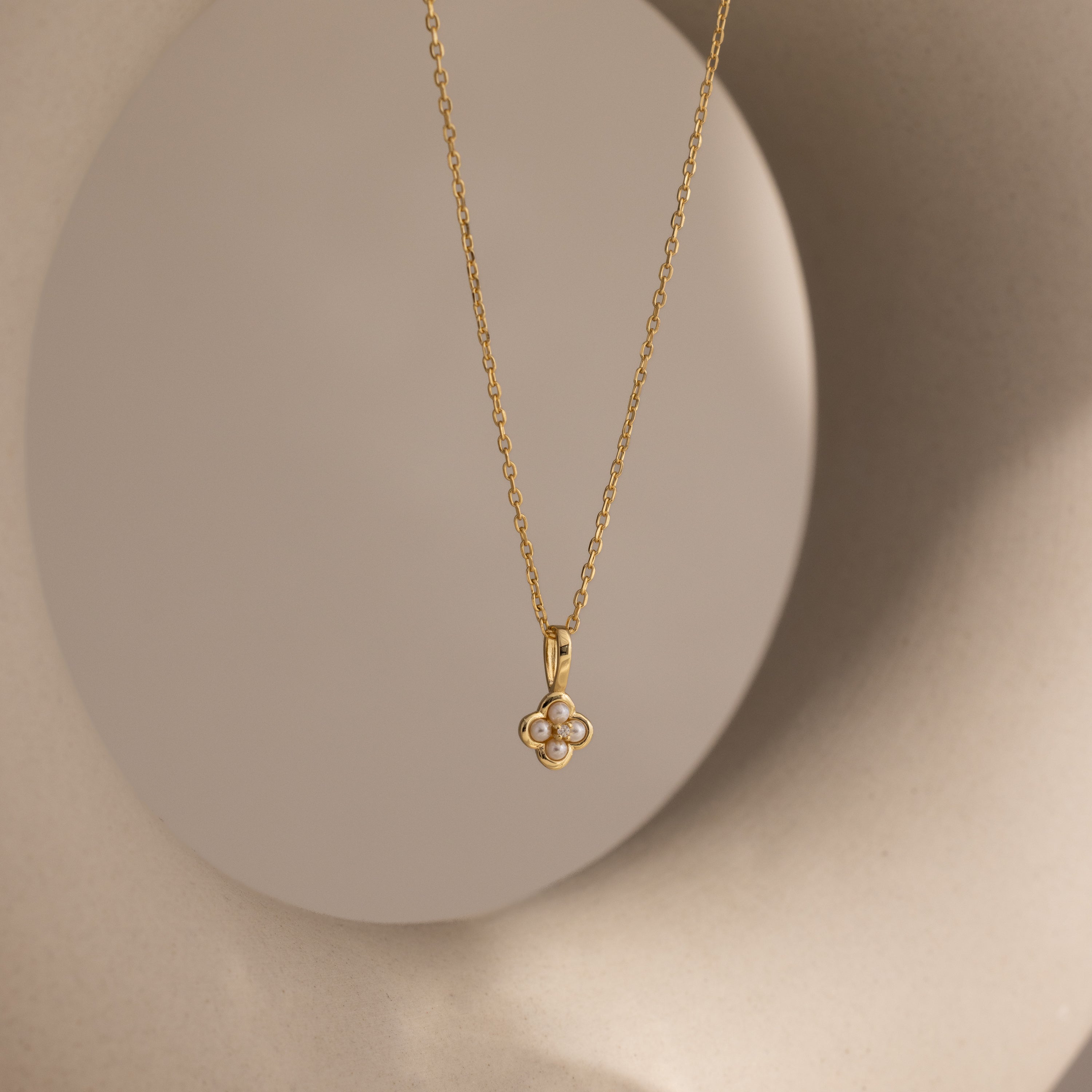 The Rounded Pearl Flower Necklace in 18K Gold features a pearl flower pendant, elegantly set against a neutral round backdrop.