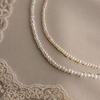 The Summer Pearl Beaded Necklace in 18K Gold rests on a beige surface with lace corners—a modern pearl jewelry piece, perfect for summer.