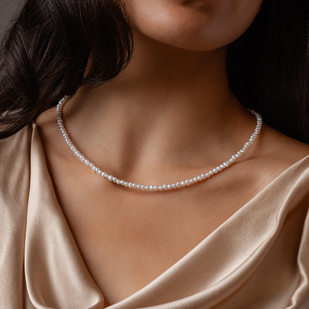 A woman wears the Summer Pearl Beaded Necklace in 18K Gold, styled with a silky, champagne-colored draped top.