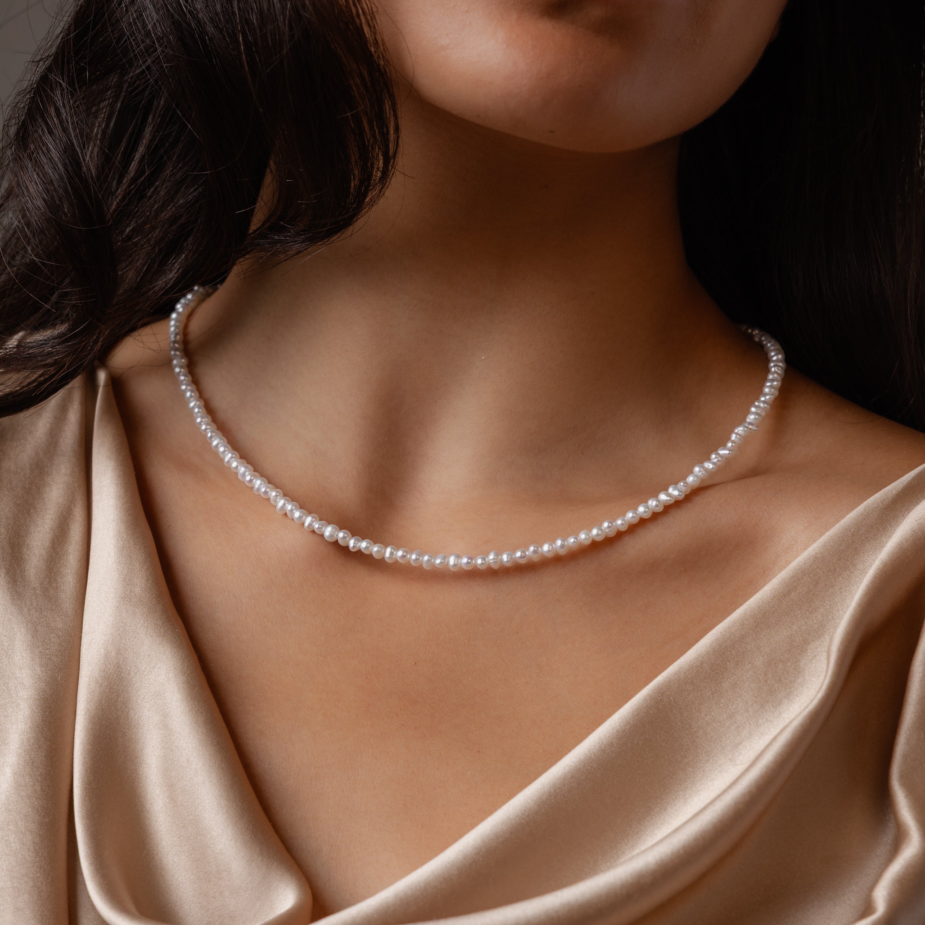 A woman showcases the Summer Pearl Beaded Necklace in Sterling Silver, paired with a champagne satin top that highlights her neck and collarbone.
