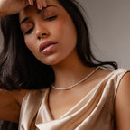 Woman in a satin dress with eyes closed wears the Summer Pearl Beaded Necklace, her hand gently resting on her forehead.
