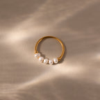 The Beaded Pearl Ring features five small white pearls set in gold, elegantly displayed on a light beige surface under soft, natural lighting for a timeless look.