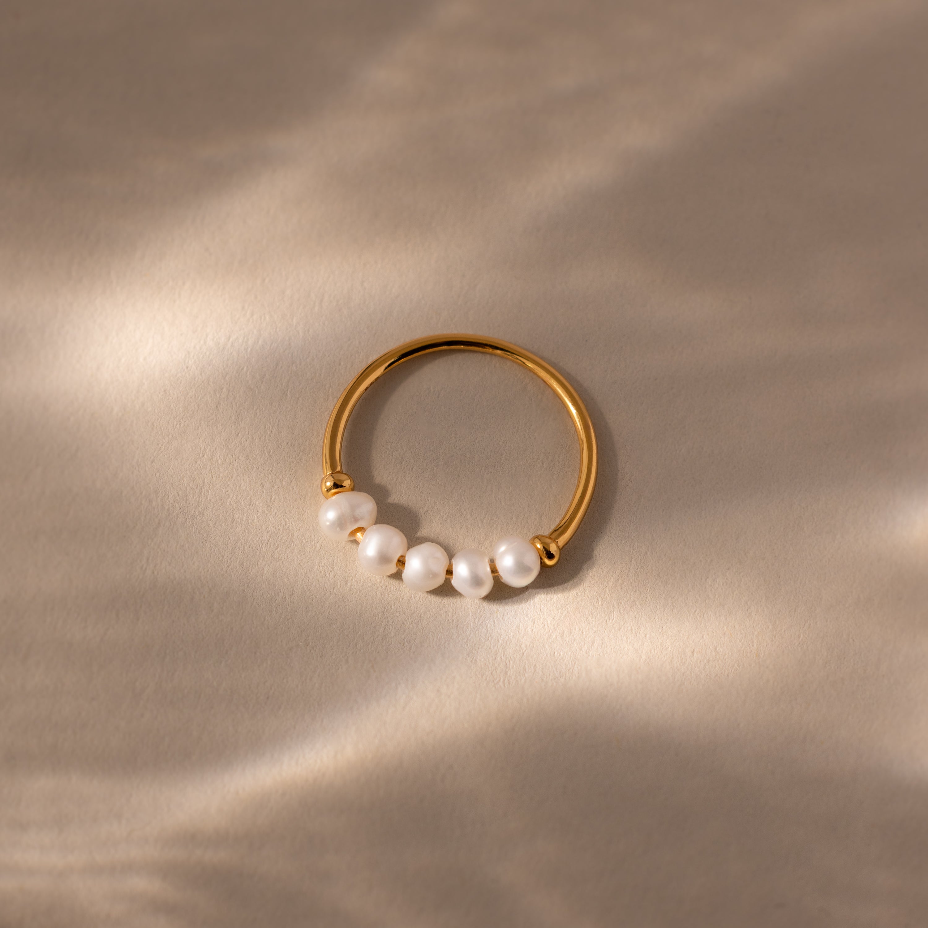 The Beaded Pearl Ring features five small white pearls set in gold, elegantly displayed on a light beige surface under soft, natural lighting for a timeless look.