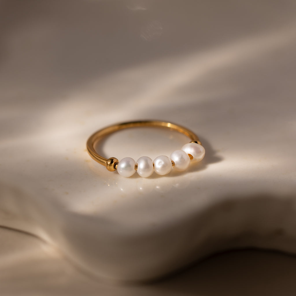 The Beaded Pearl Ring features five white pearls, displayed on a softly lit, creamy textured surface—an exquisite and elegant jewelry piece.