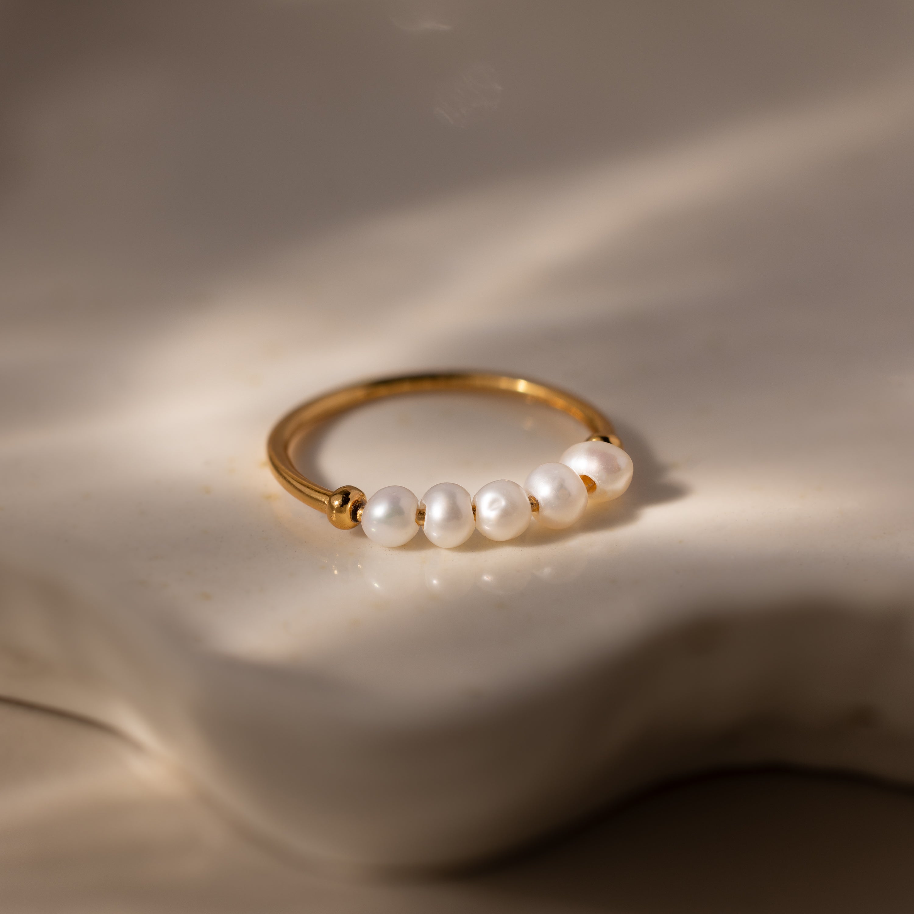 The Beaded Pearl Ring features five white pearls, displayed on a softly lit, creamy textured surface—an exquisite and elegant jewelry piece.