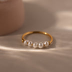 The Beaded Pearl Ring, featuring five white pearls, lies on a soft beige surface in natural light—an elegant and exquisite jewelry piece.