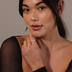 A woman with long dark hair in a sheer black top touches her face, elegantly showcasing the Beaded Pearl Ring on her finger.