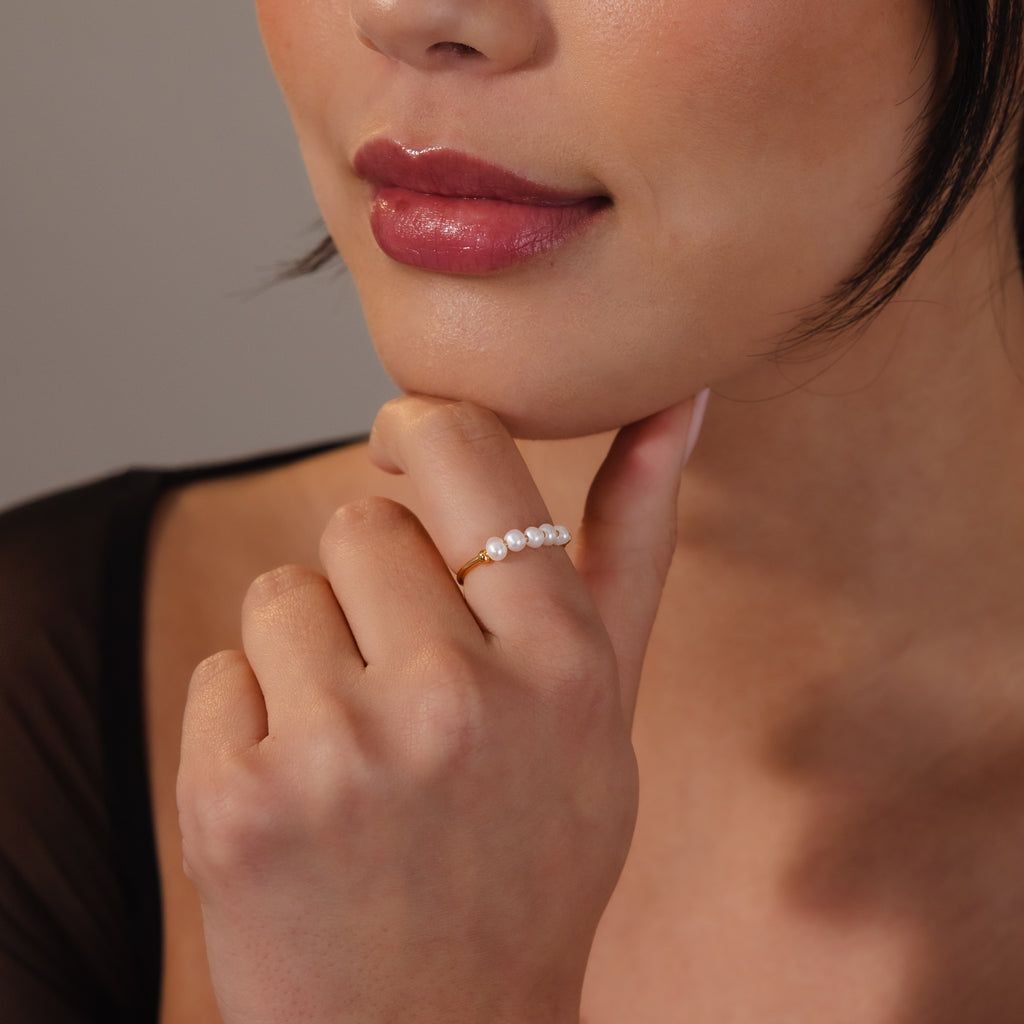 A woman touches her chin, lips slightly parted and softly lit, wearing the Beaded Pearl Ring—an elegant gold ring adorned with five lustrous pearls.