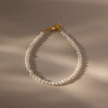 The Venus Pearl Bracelet features freshwater pearls and a gold clasp, displayed in a loose oval on a beige surface with soft lighting—an elegant accessory perfect for any occasion.
